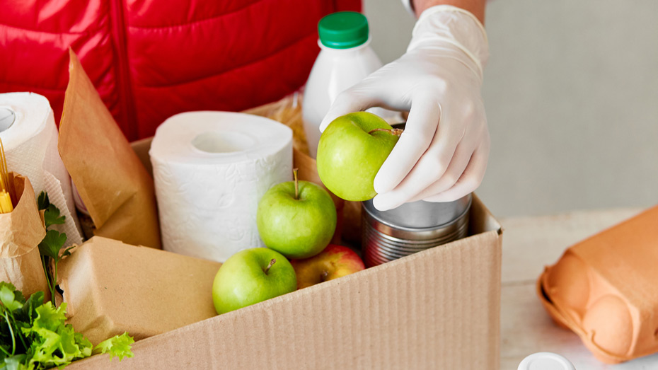 Pessoa de colete vermelho separa alimentos em caixa de mercado.